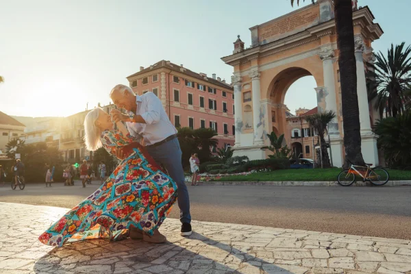 Una coppia di anziani balla felicemente davanti a un arco monumentale al tramonto.
