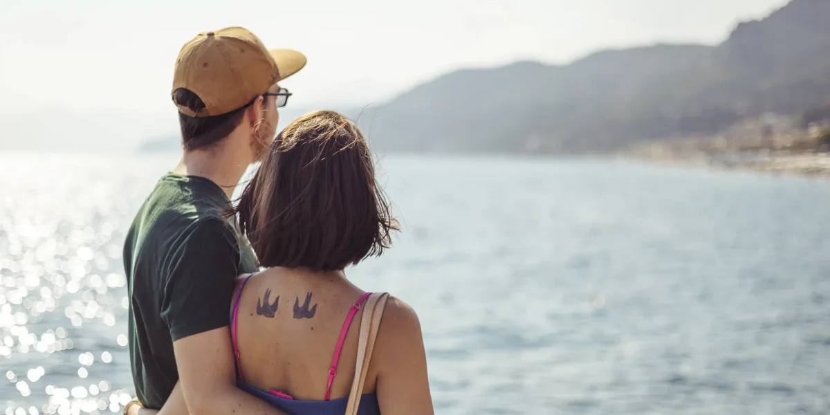 Una coppia abbracciata osserva il mare scintillante con le montagne sullo sfondo.