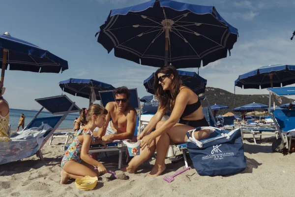 Famiglia che gioca sulla spiaggia sotto ombrelloni blu.